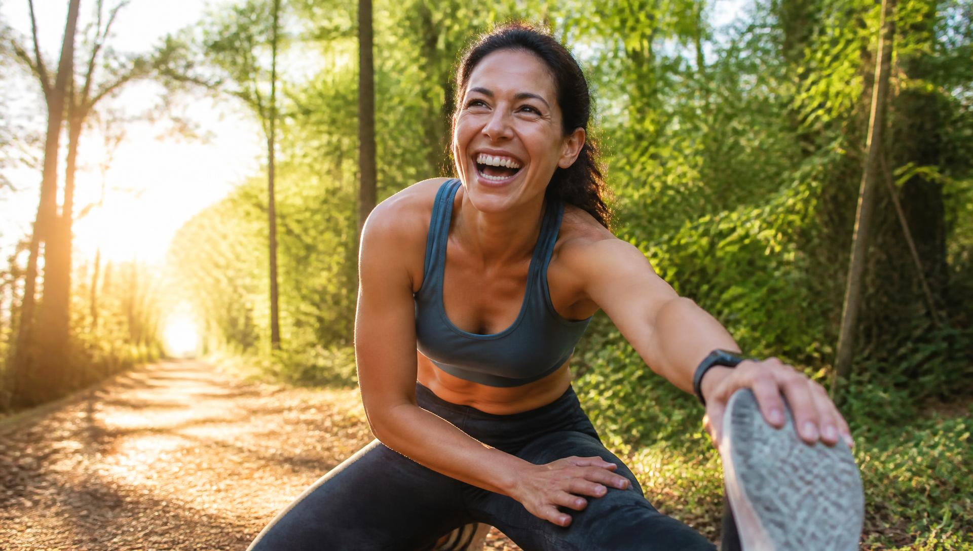 A woman stretching and laughing on a sunlit forest trail